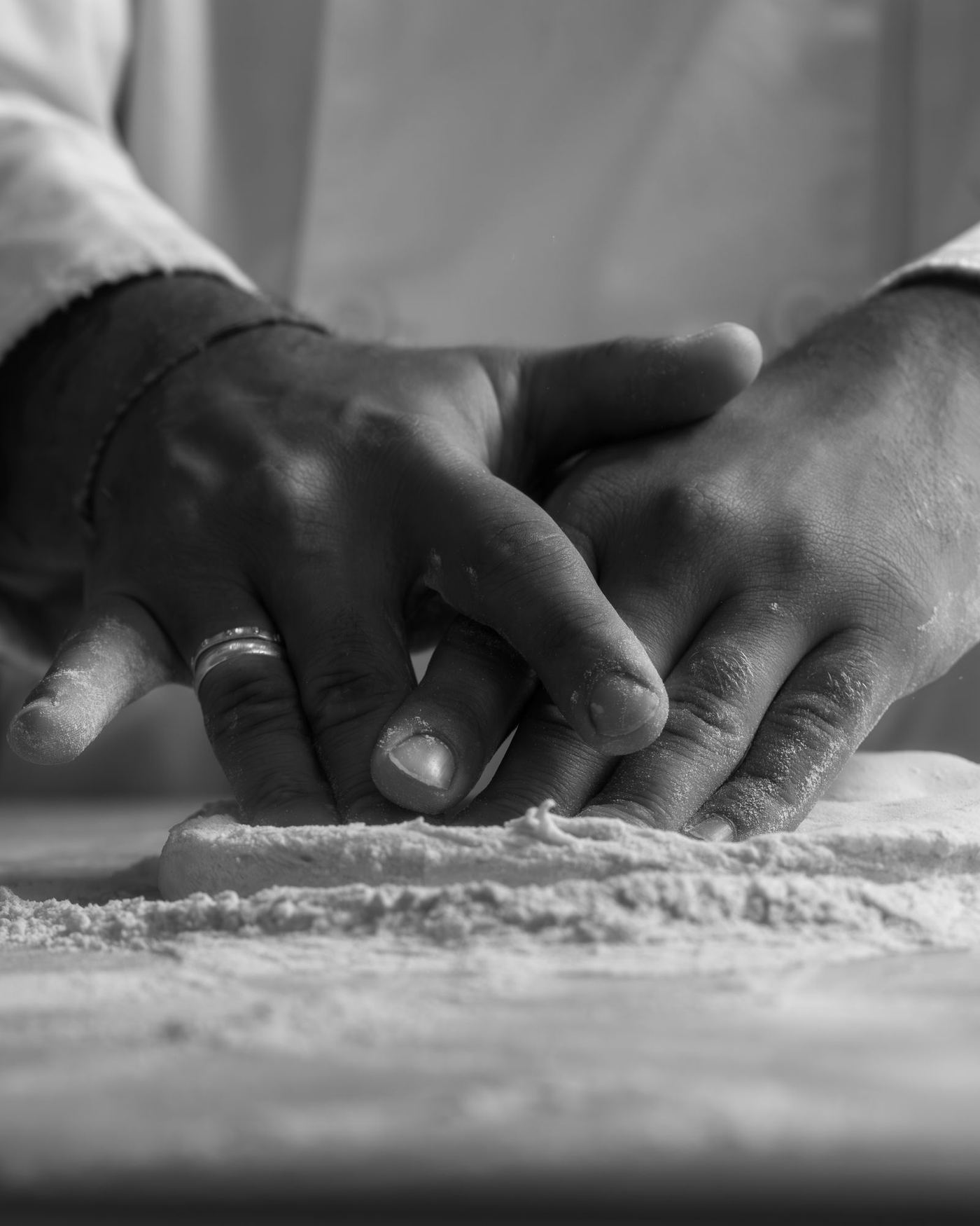 A baker's hands pressing dough on a floured bench