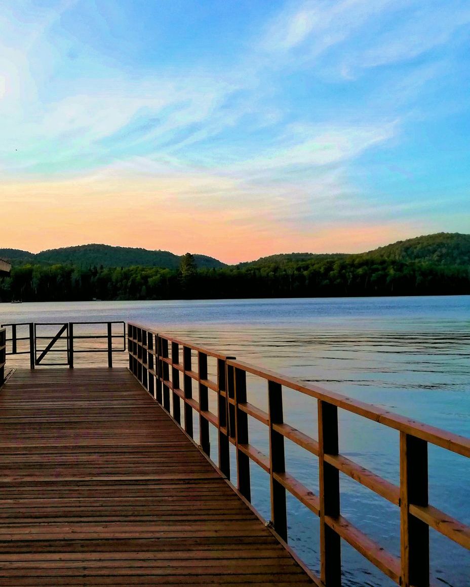 A wooden dock with a rail, over still water at dusk