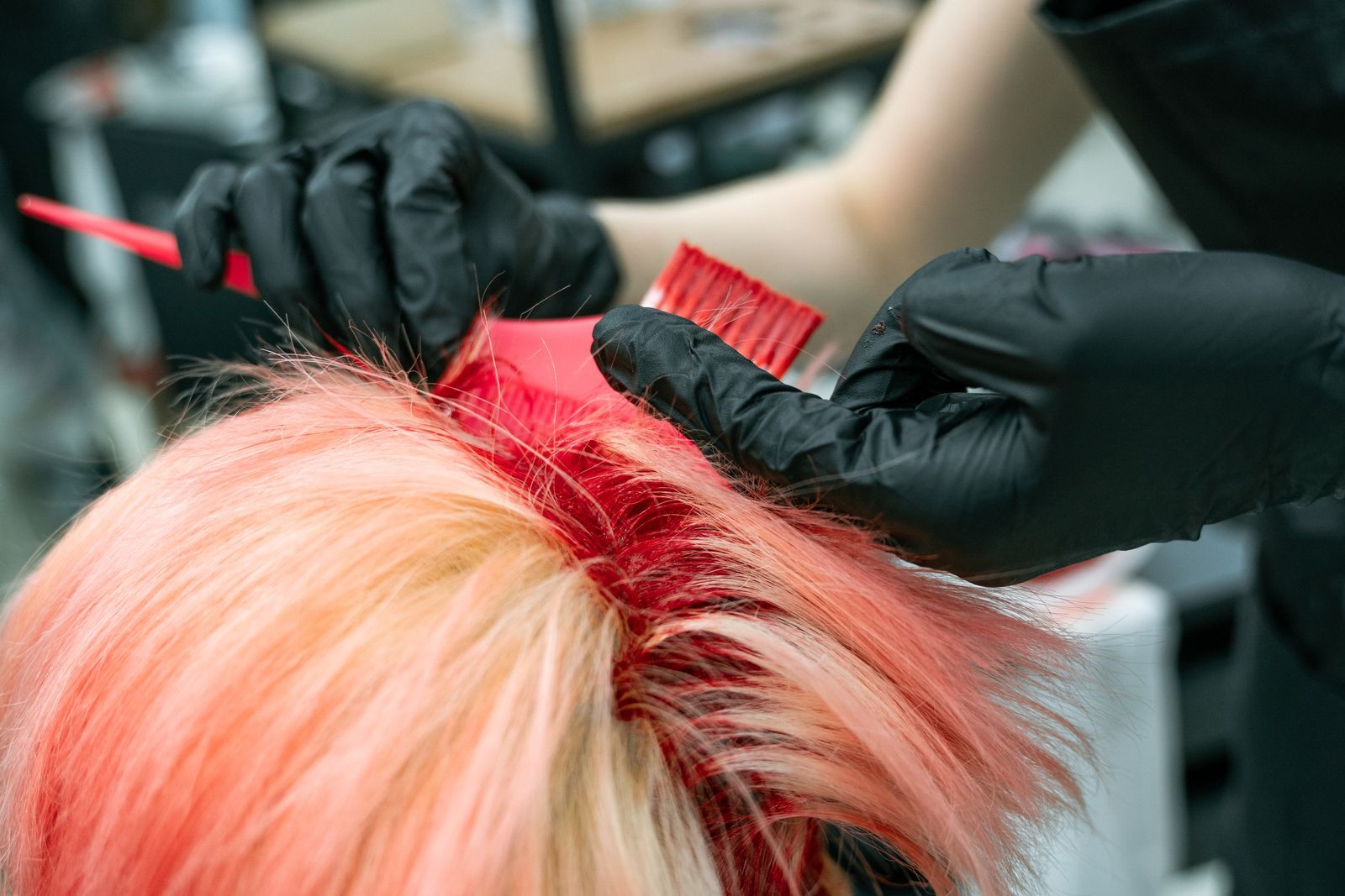 Gloved hands applying vivid pink colour to a client's hair, seen from above